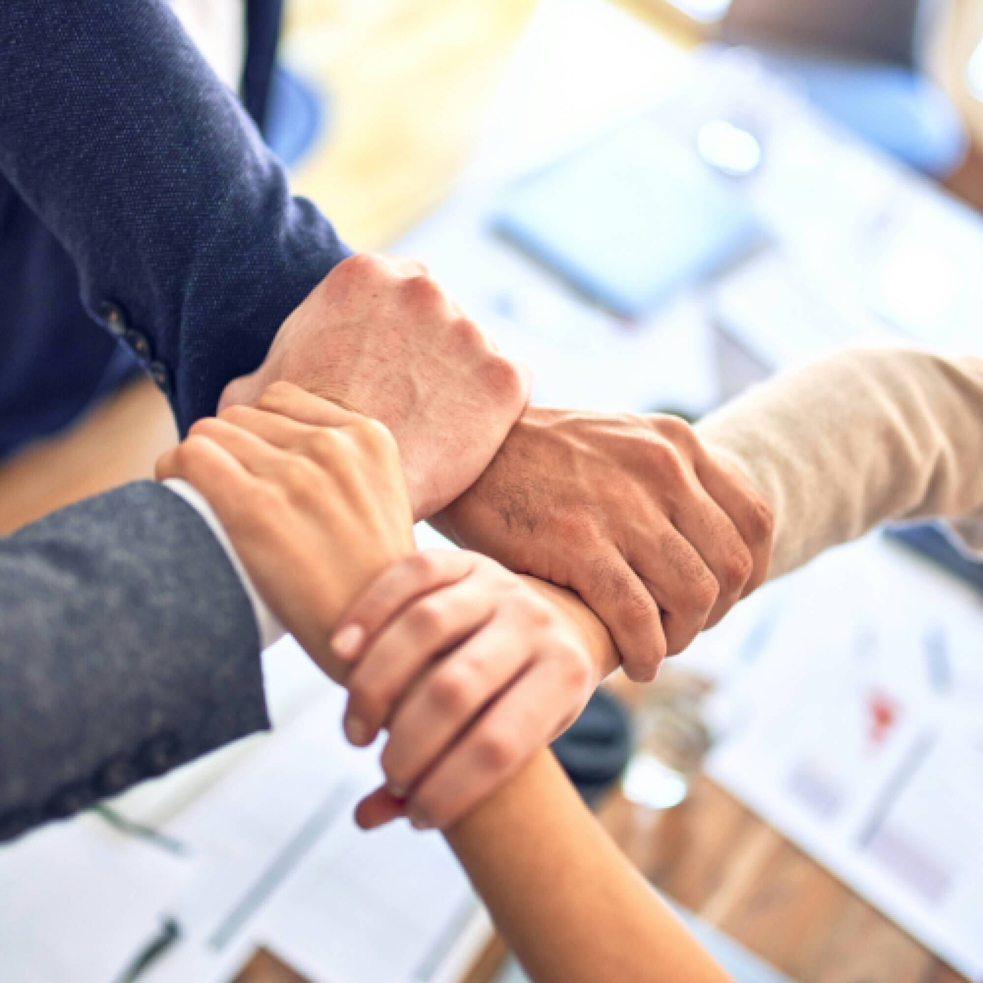 Four people linking hands to anothers wrist, making a square